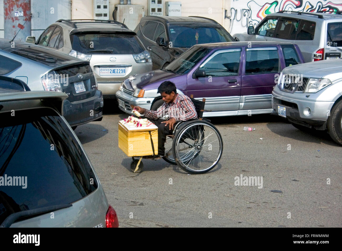 Un homme handicapé en fauteuil roulant vivant dans la pauvreté est la vente de fleurs de cérémonie sur une rue de ville de Penh, Cambodge. Banque D'Images