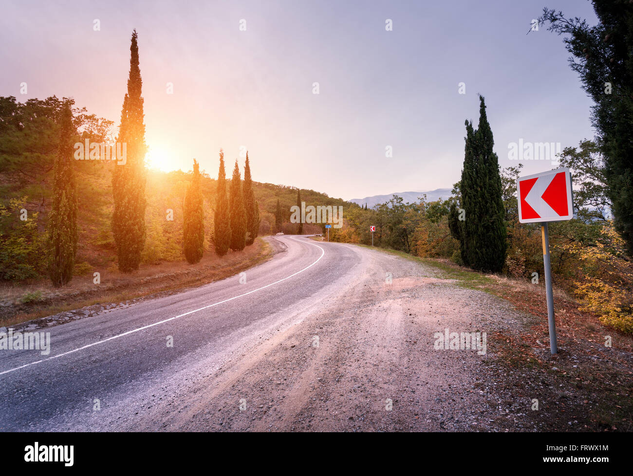 Belle route asphaltée avec signe de route dans la montagne au coucher du soleil en été. Banque D'Images