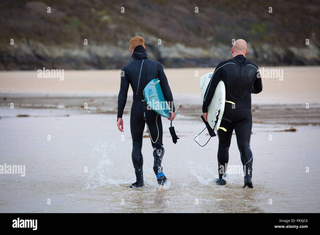 Deux surfeurs qui marchent dans leurs combinaisons en bas d'une plage. Banque D'Images