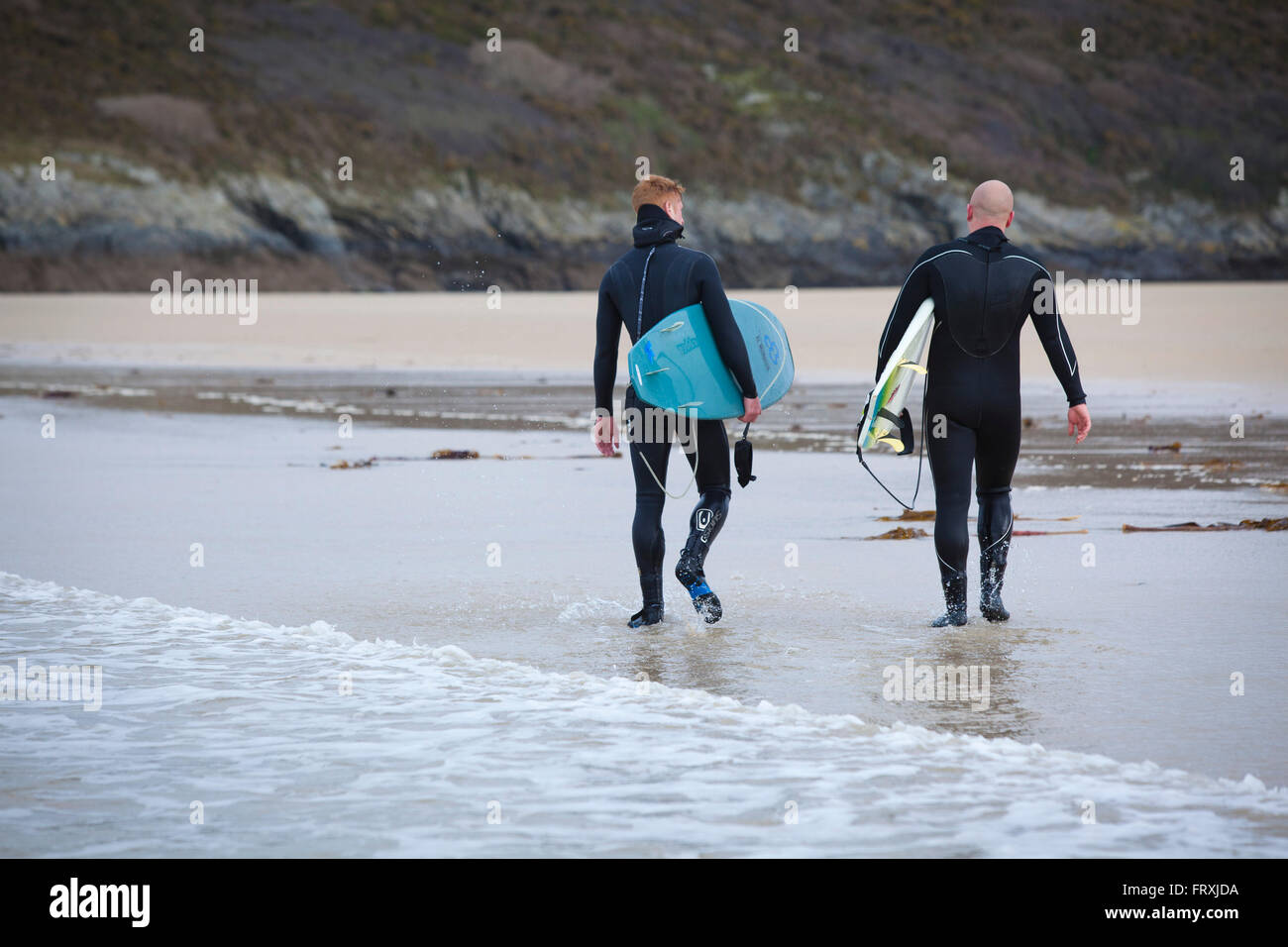 Deux surfeurs qui marchent dans leurs combinaisons en bas d'une plage. Banque D'Images