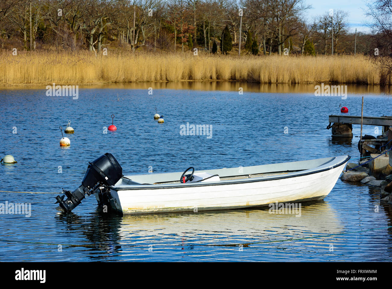 Un petit bateau à moteur hors-bord en plastique amarré dans une baie. Les bouées, l'eau de mer et Reed est dans l'arrière-plan. Un moteur de direction noir wh Banque D'Images