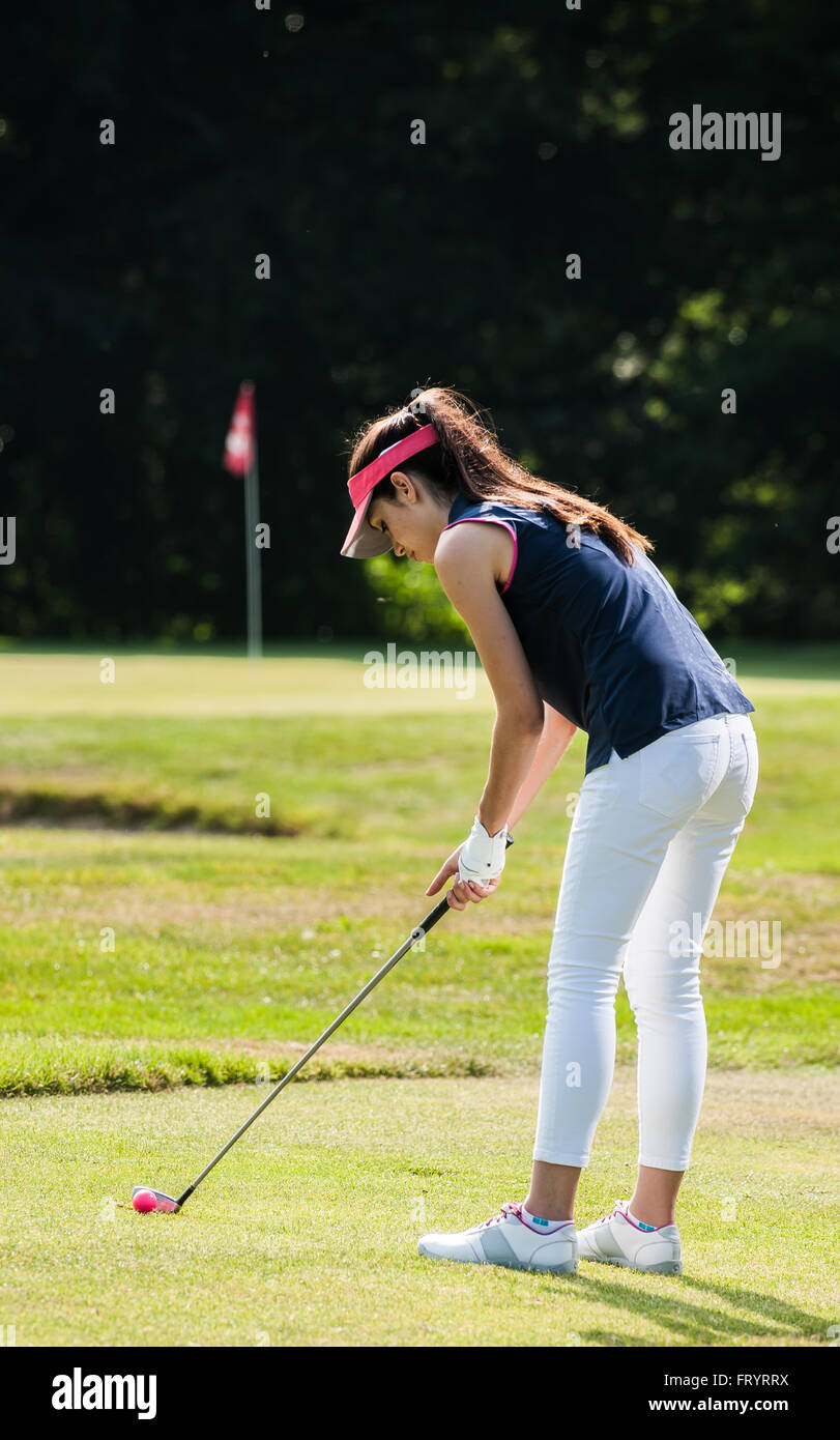 Portrait d'une jeune femme balance son club sur un parcours de golf. Elle  est debout, regardant sa balle rose portant un bonnet rouge et une tenue de  sport Photo Stock - Alamy