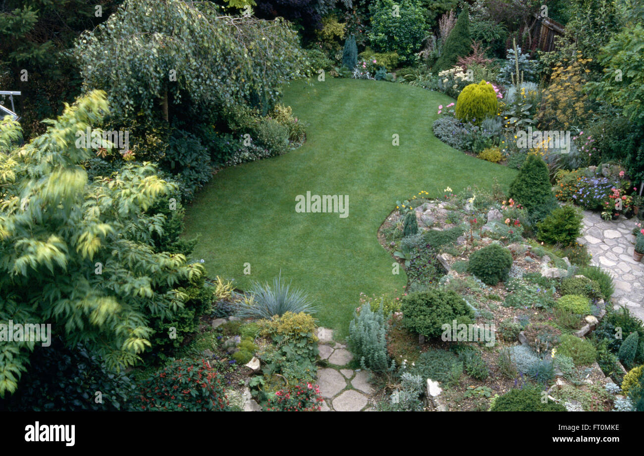 Vue d'une courbe récemment fauché pelouse bordée de frontières avec un petit bouleau et faible dans les petits conifères de rocaille Banque D'Images