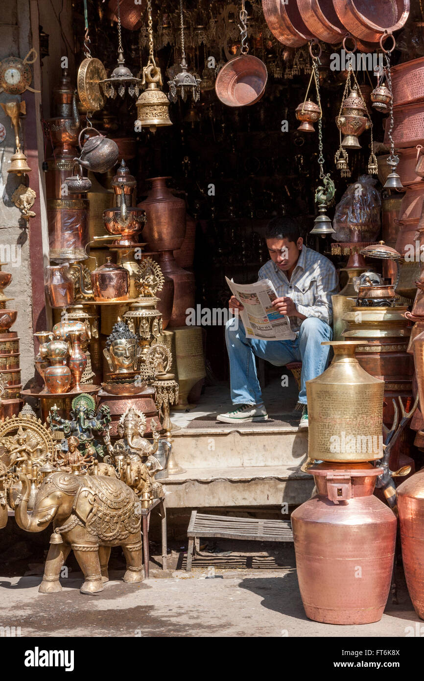 Népal, Katmandou. Vendeur d'Airain hindoue et bouddhiste d'articles de décoration et ustensiles à lire le journal. Banque D'Images