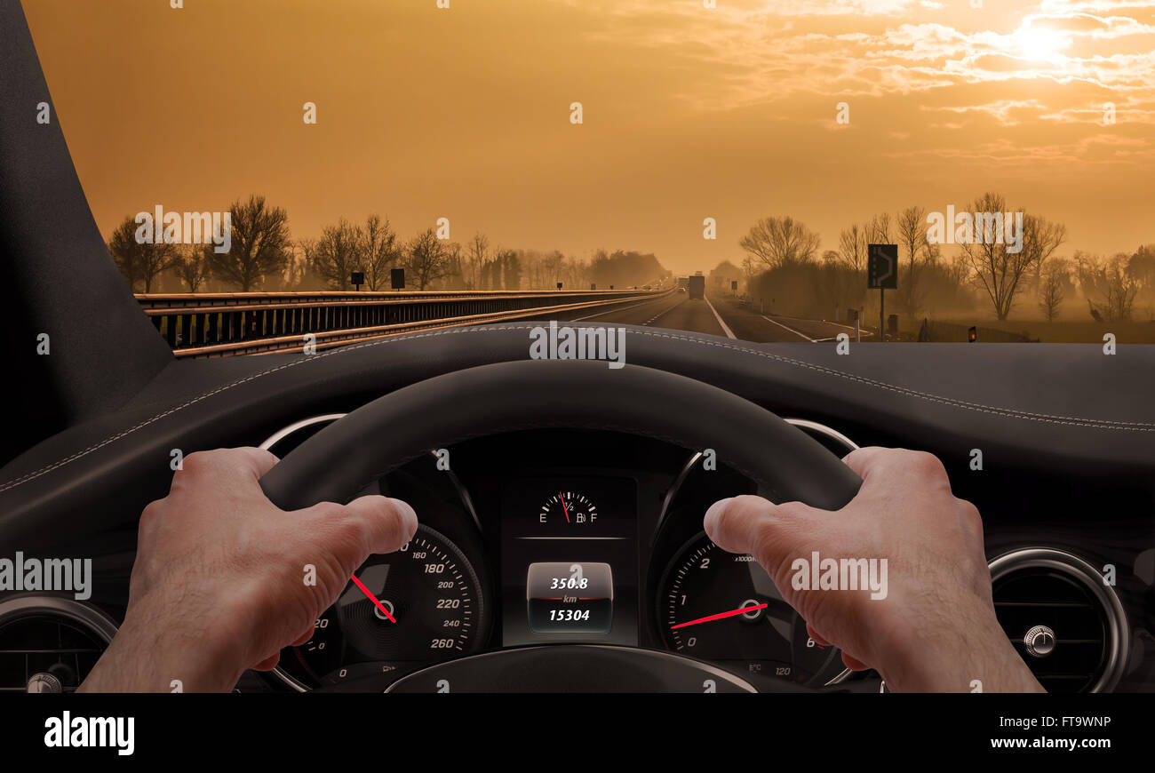 La conduite au coucher du soleil. Vue depuis l'angle du conducteur alors que les mains sur le volant. Banque D'Images