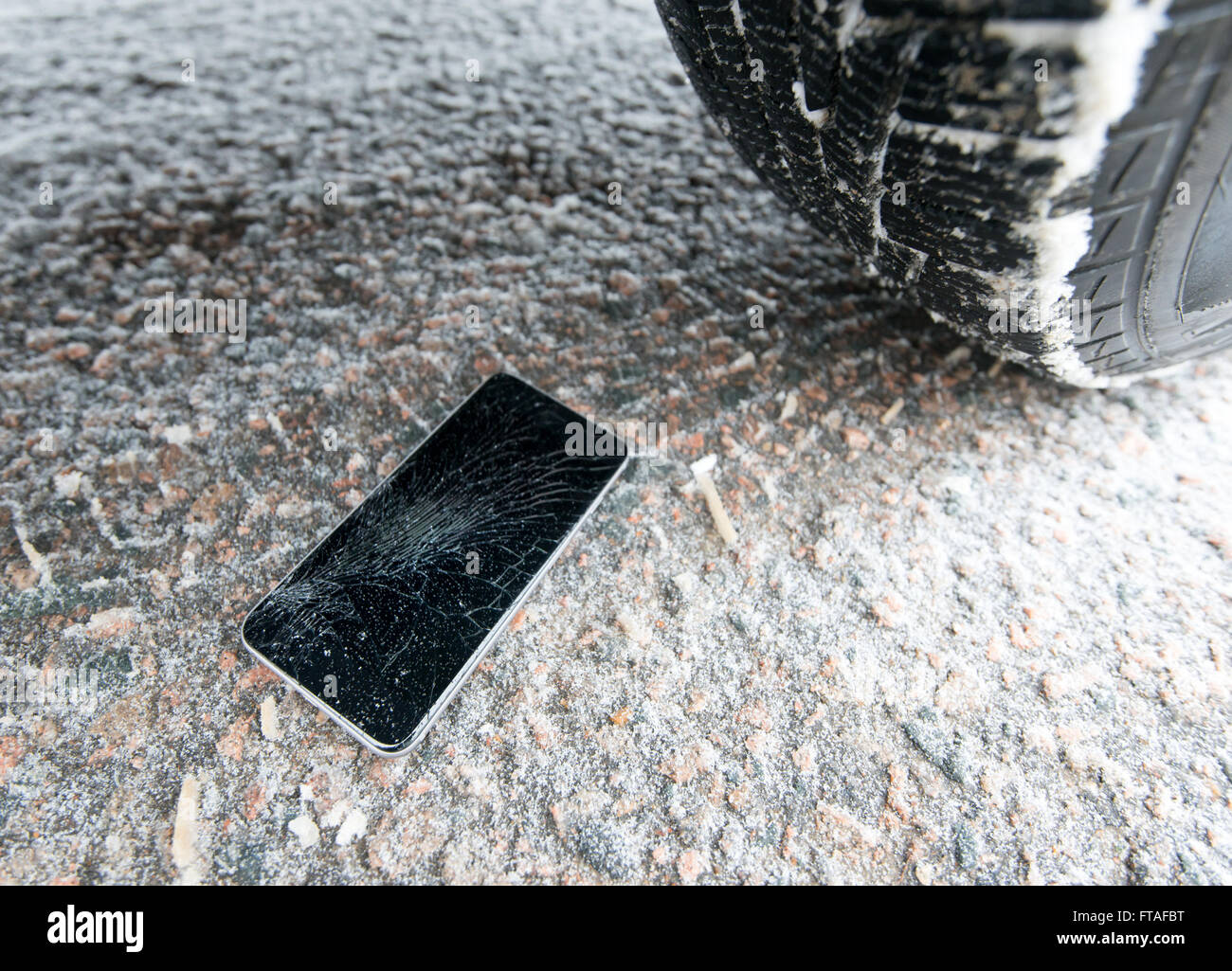 Téléphone avec écran cassé sur la neige en voiture piste. Verre recouvert de flocons de neige. Appareil écrasé par la roue. Banque D'Images