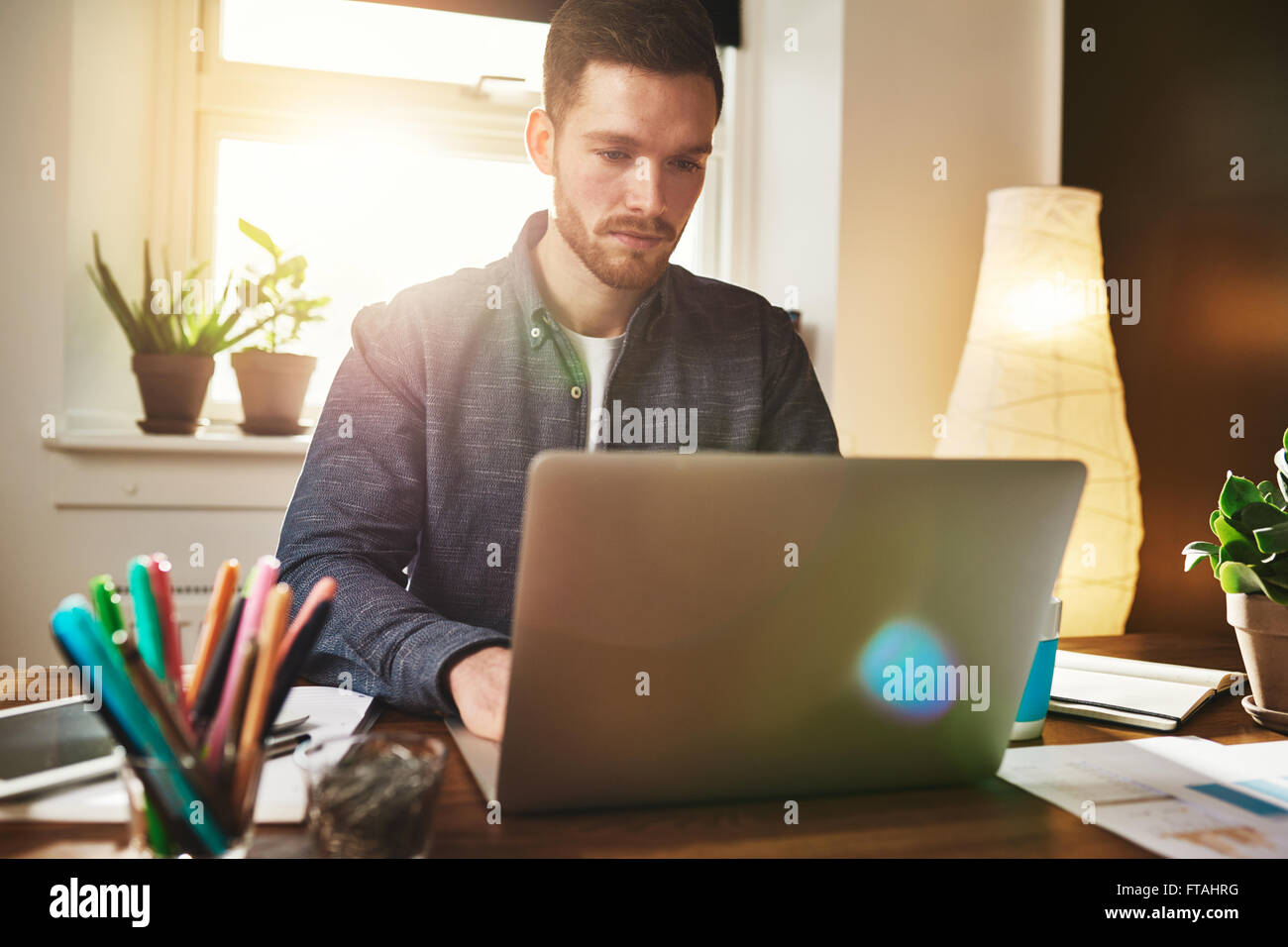 Homme d'inquiéter la lecture de données sur son ordinateur portable avec une expression solennelle comme il travaille dans son bureau à domicile, reflets colorés Banque D'Images