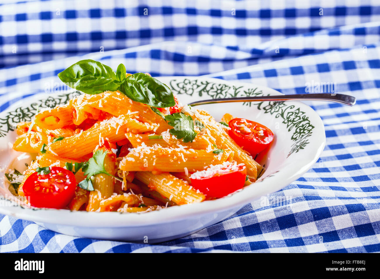 Plaque avec pene pâtes sauce bolognaise tomates cerise haut de persil et les feuilles de basilic sur nappe bleue à carreaux. L'italien et Med Banque D'Images