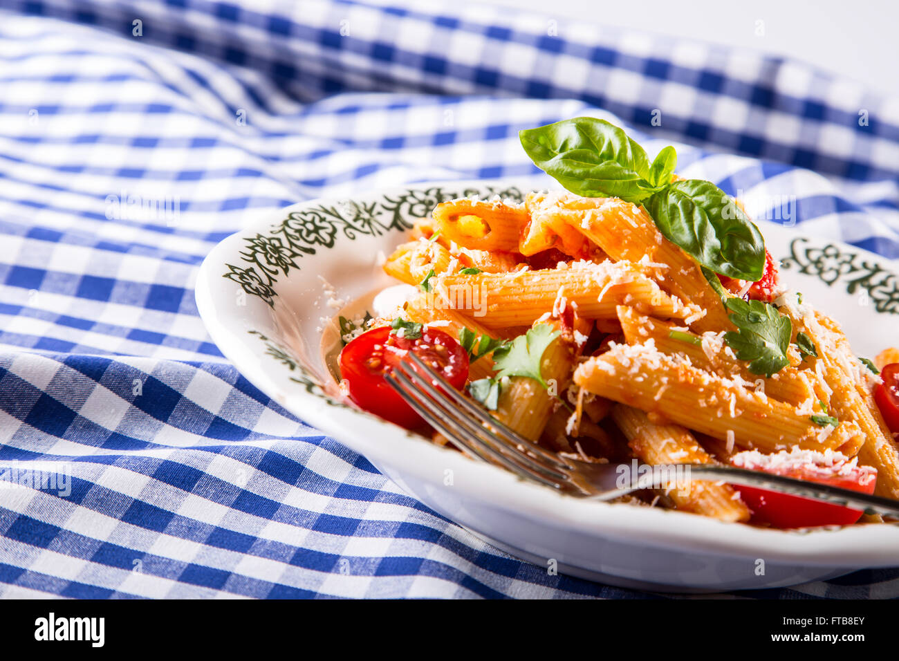 Plaque avec pene pâtes sauce bolognaise tomates cerise haut de persil et les feuilles de basilic sur nappe bleue à carreaux. L'italien et Med Banque D'Images