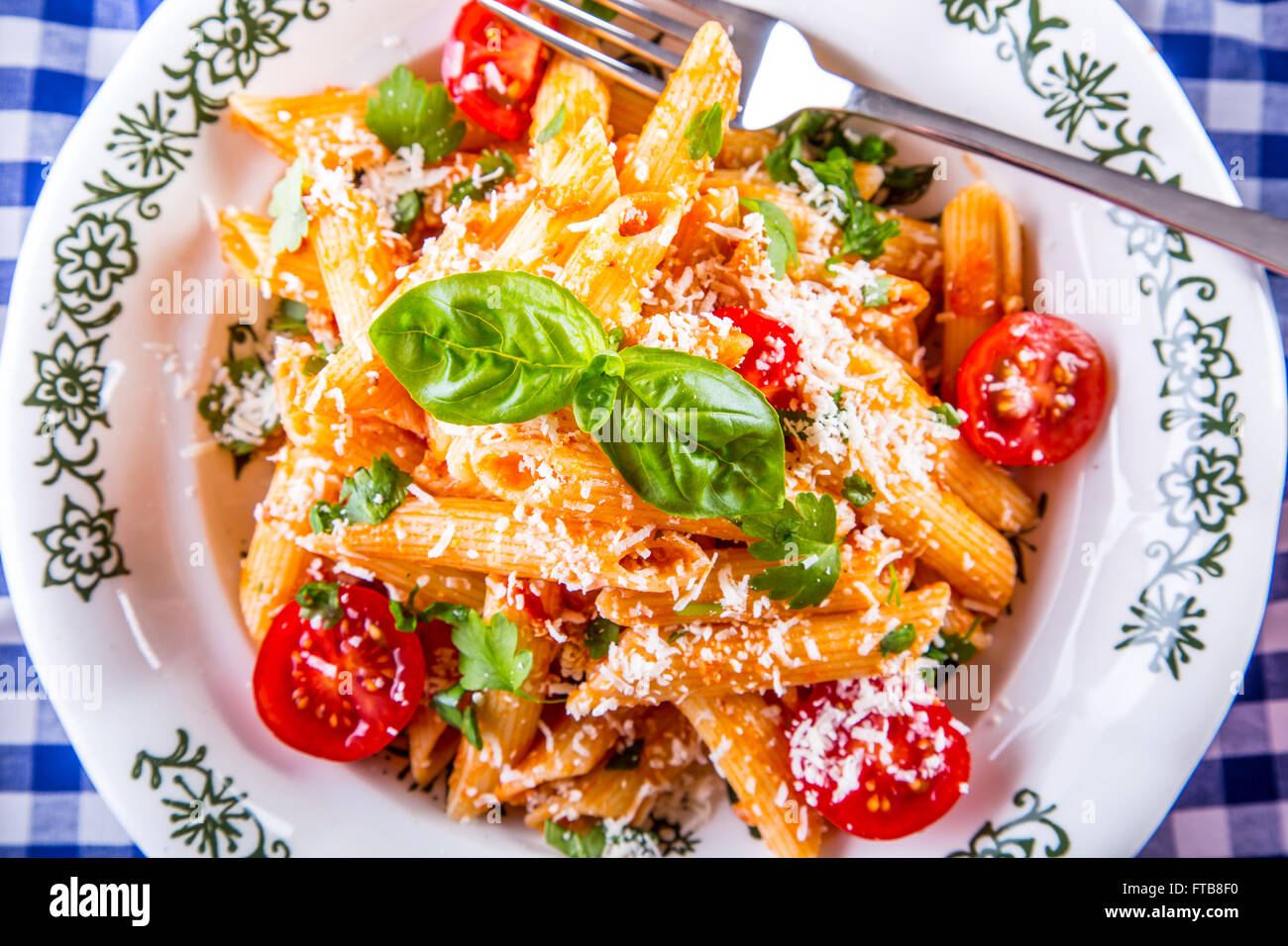 Plaque avec pene pâtes sauce bolognaise tomates cerise haut de persil et les feuilles de basilic sur nappe bleue à carreaux. L'italien et Med Banque D'Images
