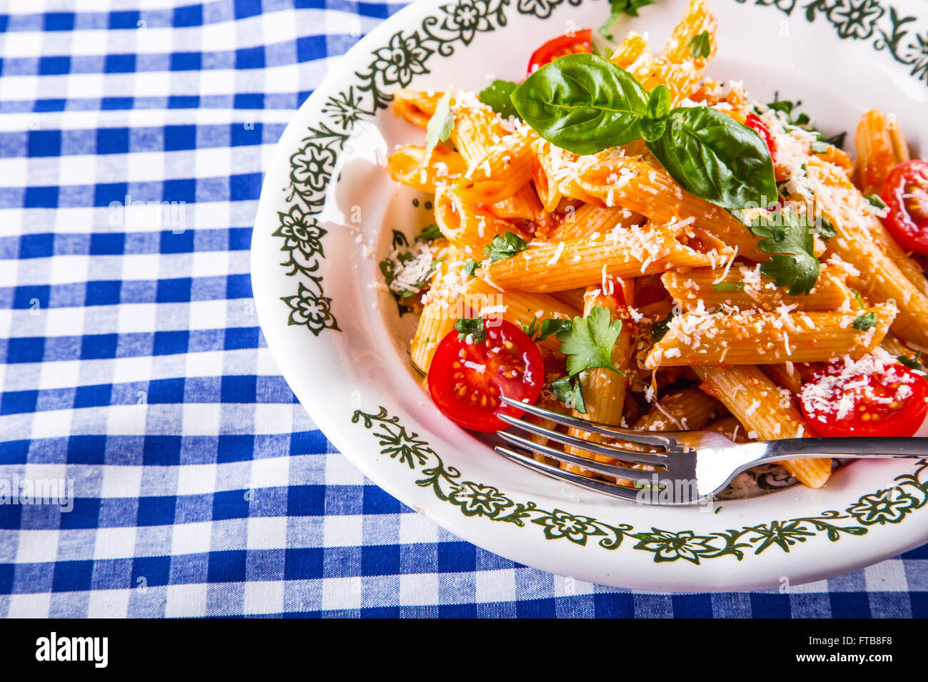 Plaque avec pene pâtes sauce bolognaise tomates cerise haut de persil et les feuilles de basilic sur nappe bleue à carreaux. L'italien et Med Banque D'Images