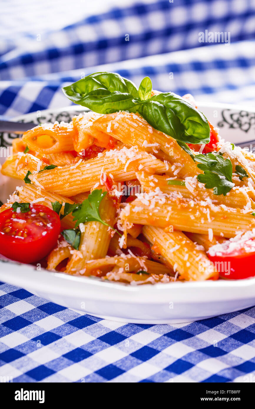 Plaque avec pene pâtes sauce bolognaise tomates cerise haut de persil et les feuilles de basilic sur nappe bleue à carreaux. L'italien et Med Banque D'Images