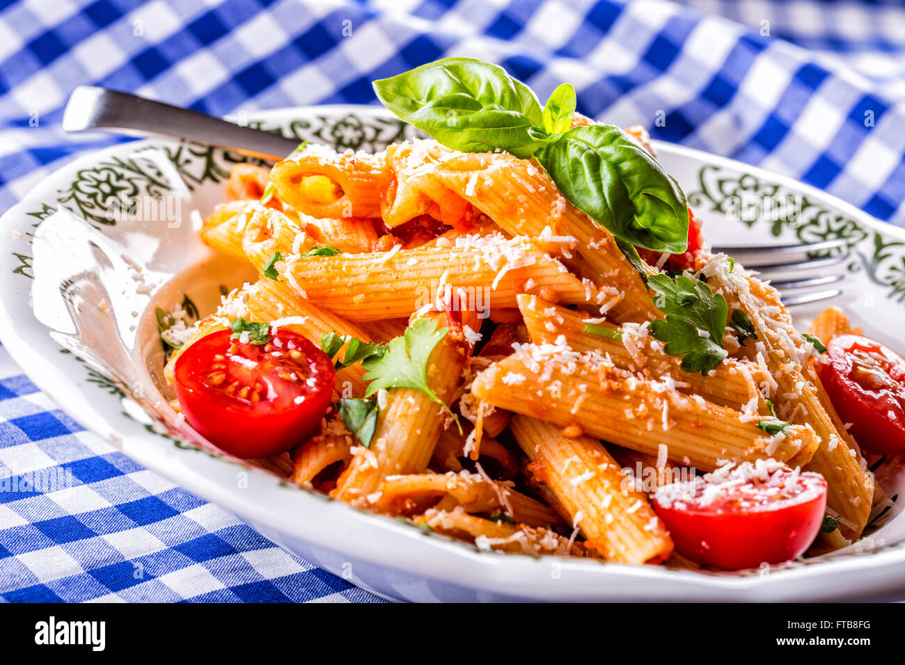 Plaque avec pene pâtes sauce bolognaise tomates cerise haut de persil et les feuilles de basilic sur nappe bleue à carreaux. L'italien et Med Banque D'Images