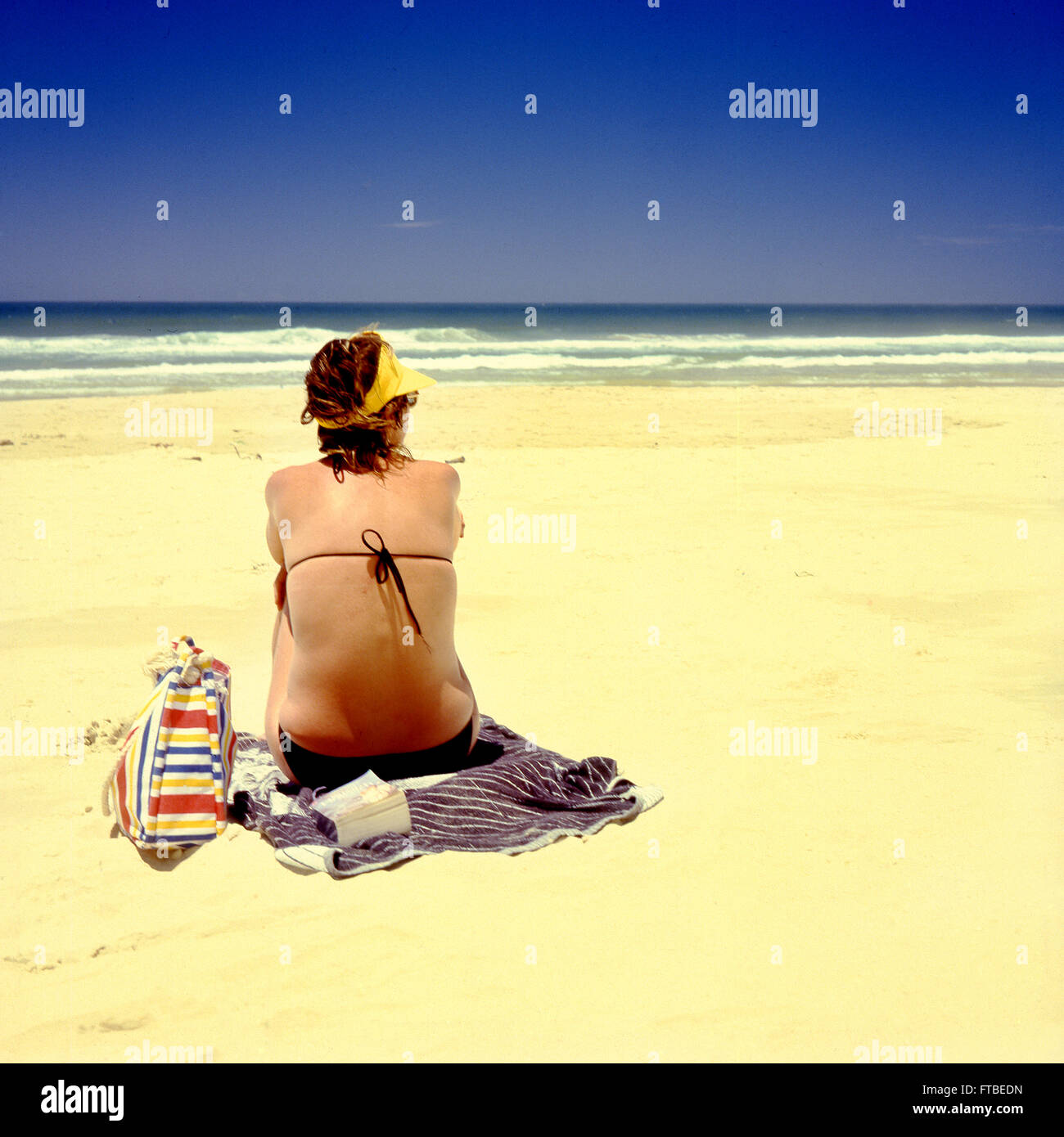 Woman in bikini assis sur une plage de sable avec ciel bleu clair. L'espace pour le texte. Banque D'Images