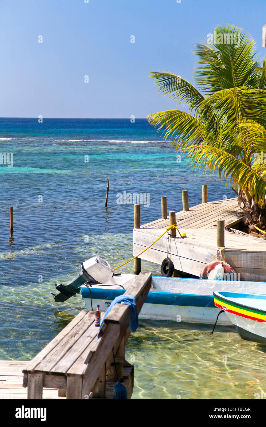 Littoral tropical avec des bateaux colorés amarrés à un quai en bois avec des palmiers se balançant dans la brise Banque D'Images