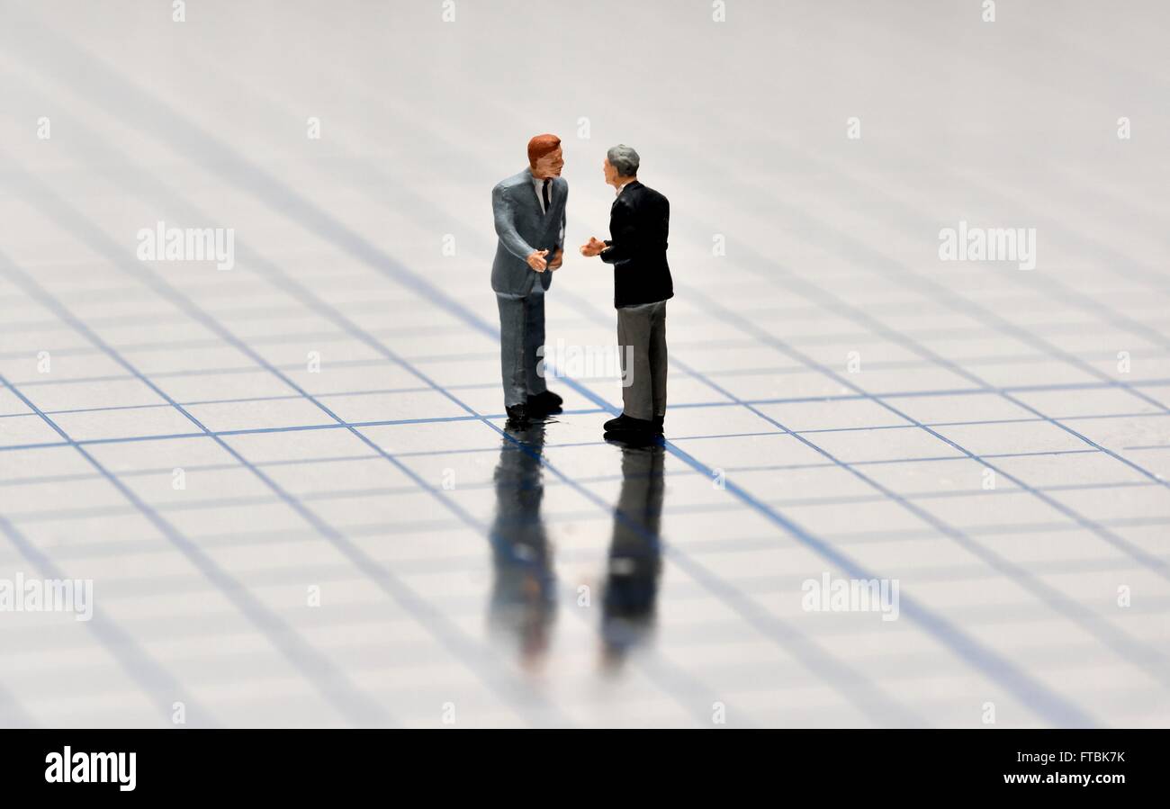 Figurine miniature businessmen having a conversation sur une surface brillante au carré bleu. Banque D'Images