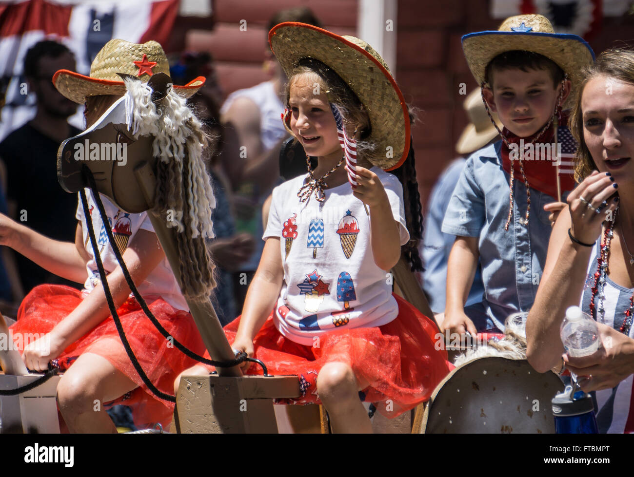 Graeagle, Californie, USA- Enfants équitation seesaw chevaux à bascule et agitaient des drapeaux qu'ils montent dans un défilé du 4 juillet. Banque D'Images