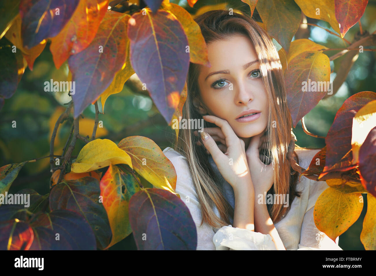 Belle jeune femme posant parmi les feuilles aux couleurs automnales Banque D'Images