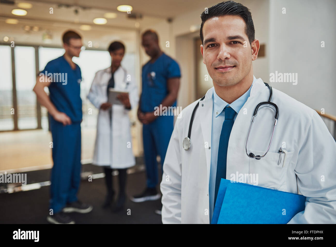 Smiling doctor wearing white jacket et stéthoscope avec trois collègues en arrière-plan Banque D'Images