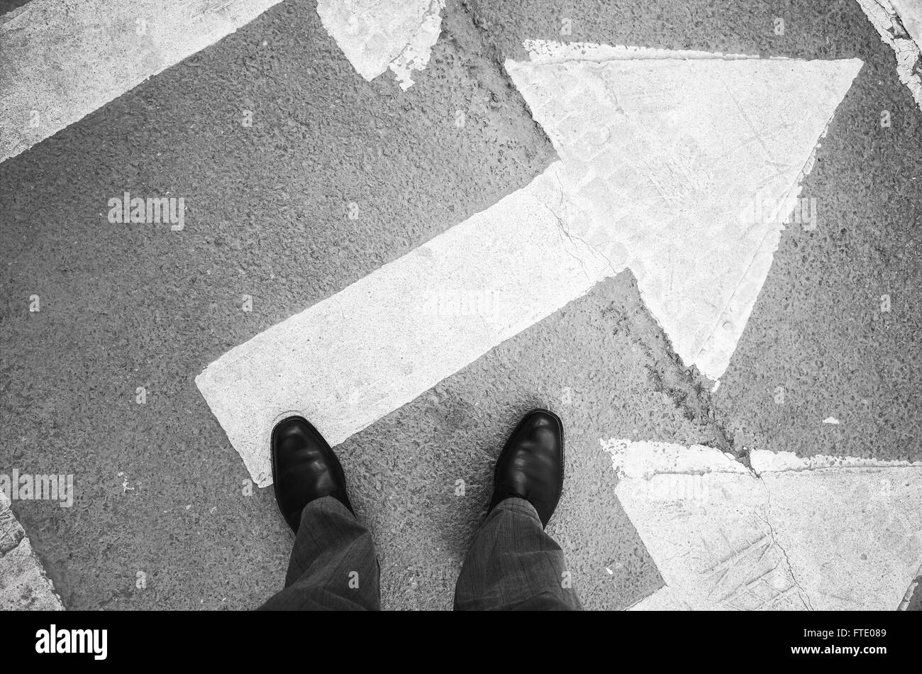 L'homme citadin en noir chaussures en cuir brillant nouveau comité permanent sur le passage pour piétons, signalisation par des flèches blanches Banque D'Images