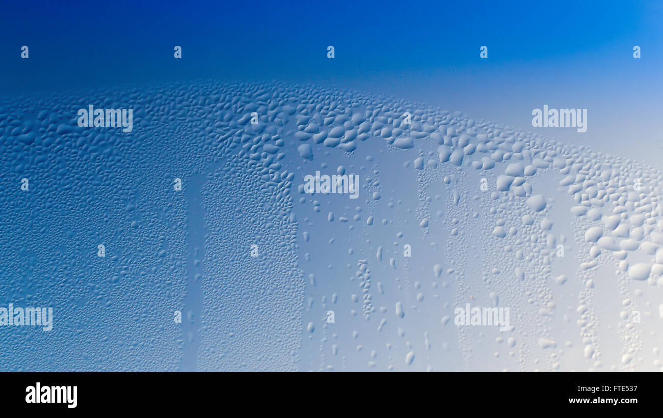 La Condensation forme des gouttelettes d'eau sur la surface d'une fenêtre en verre clair de l'intérieur de la chambre. Sombre ciel bleu couleur texture Banque D'Images