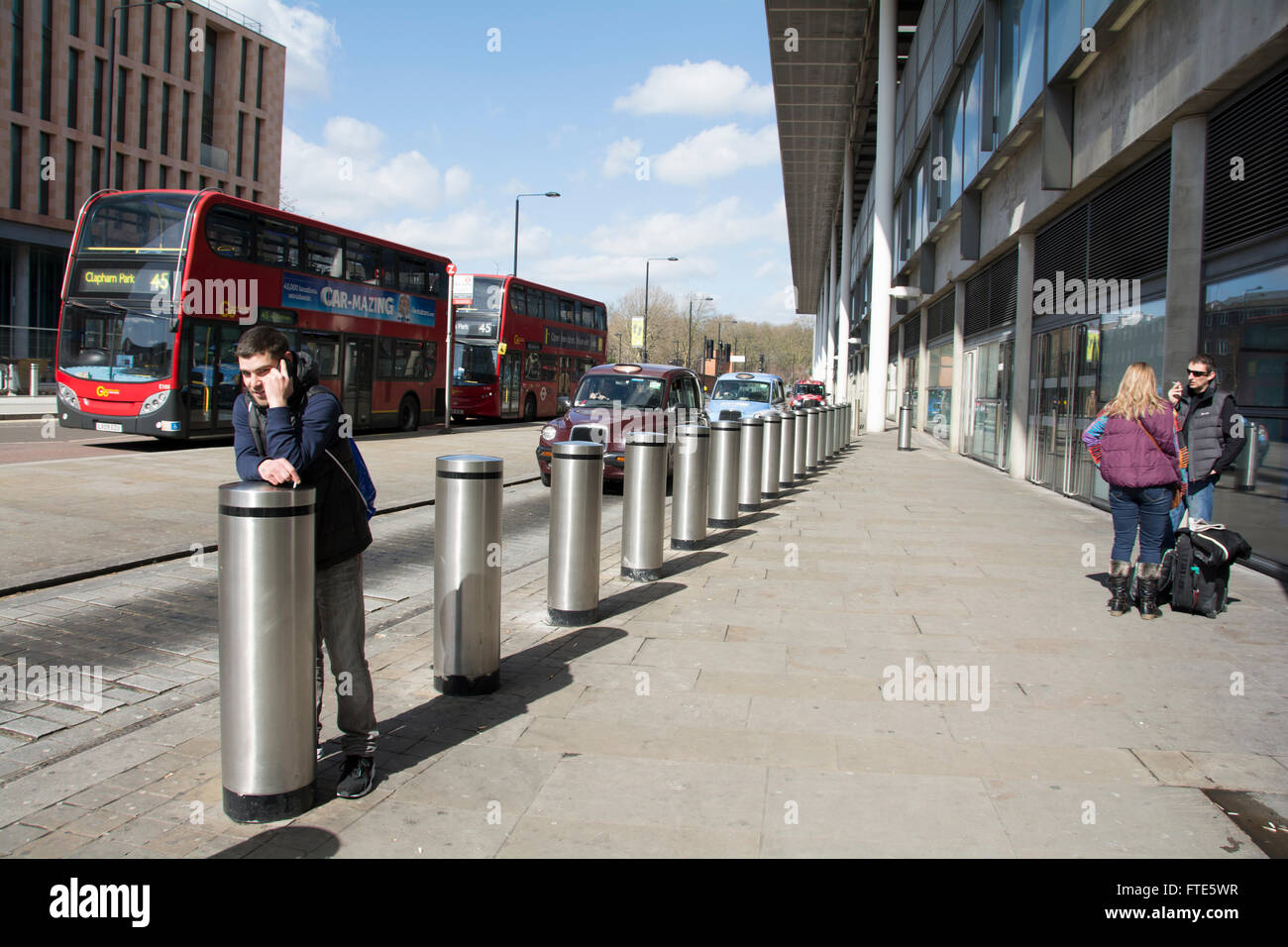 Jeune homme parle sur téléphone mobile tout en s'appuyant sur des bornes de sécurité à l'extérieur de la gare St Pancras à Londres, Royaume-Uni Banque D'Images