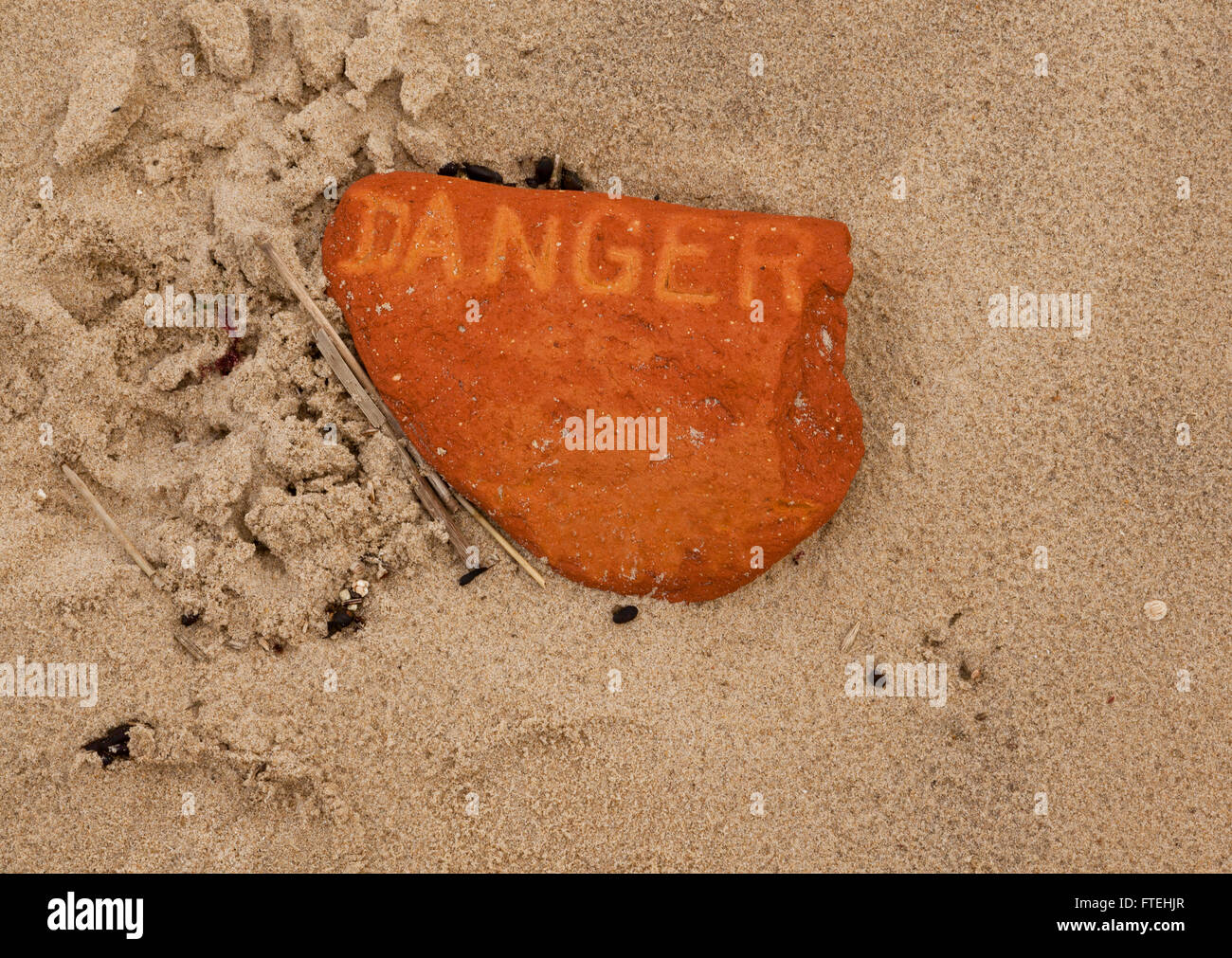 Le mot "danger" imprimé sur un morceau d'une brique dans le sable d'une plage Banque D'Images