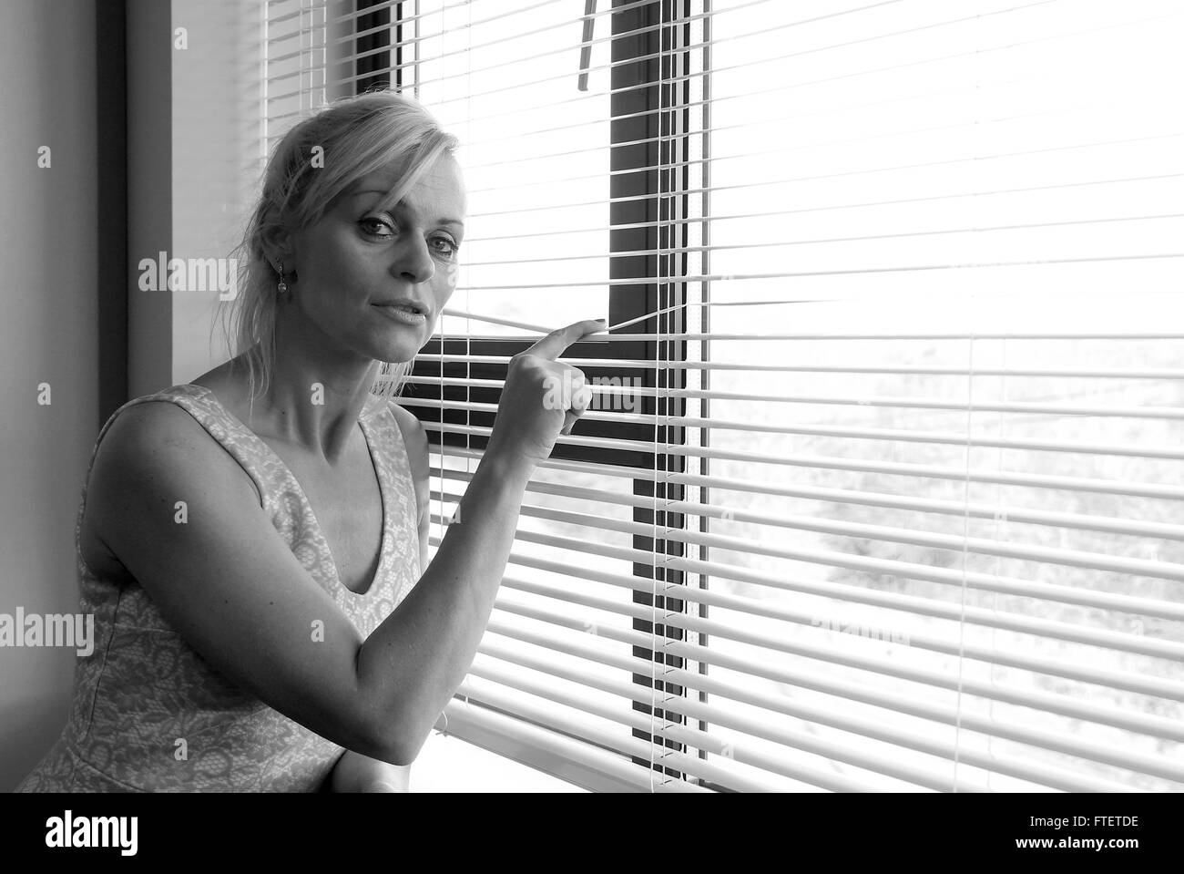 Belle blonde mature femme d'Europe de l'est à l'expectative à travers les stores vénitiens. 2 Janvier 2015 Banque D'Images