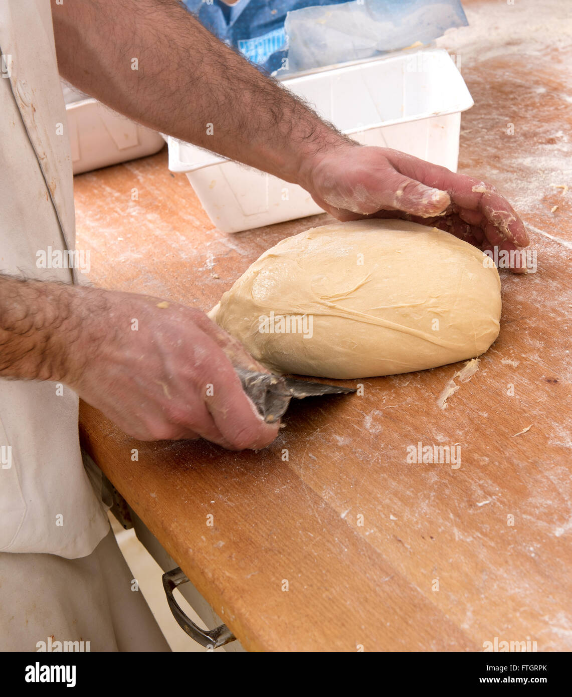 Baker la préparation d'une miche de pain à l'aide d'un racloir et sa main pour façonner et former la pâte sur un comptoir en bois Banque D'Images