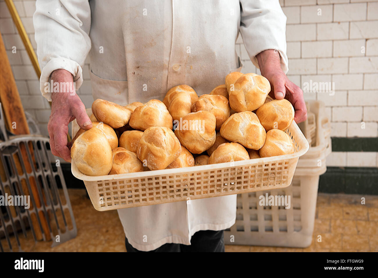 Baker tenant un panier plein de petits pains blanc croustillant dans son manteau blanc à la boulangerie Banque D'Images