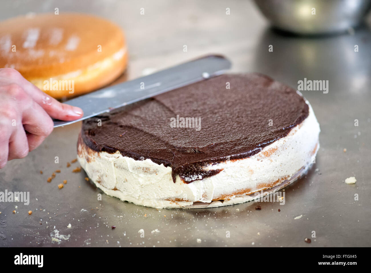 Boulanger pâtissier ou un glaçage du gâteau au chocolat à l'aide d'une grande spatule plate comme il travaille dans une boulangerie Banque D'Images
