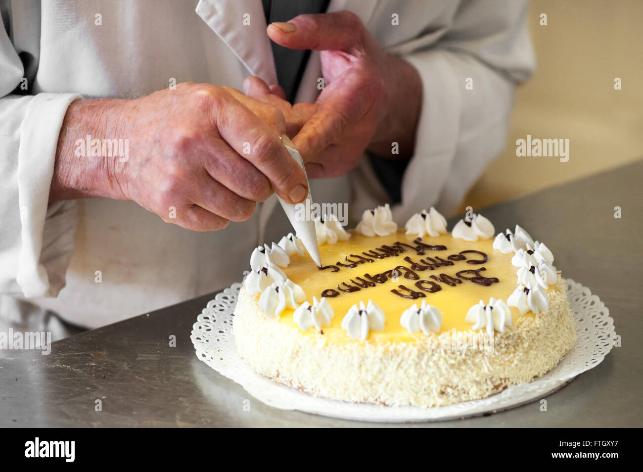 Close Up of Male Baker écrit un message de célébration sur le dessus de gâteau au citron Banque D'Images