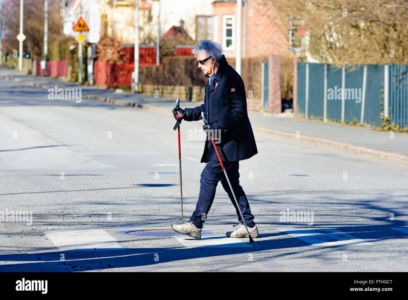 L'ahus, Suède - 20 mars 2016 : Senior woman out marcher avec les bâtons de marche. Elle est traversée d'une rue. Pas de voitures visibles. Peo réel Banque D'Images