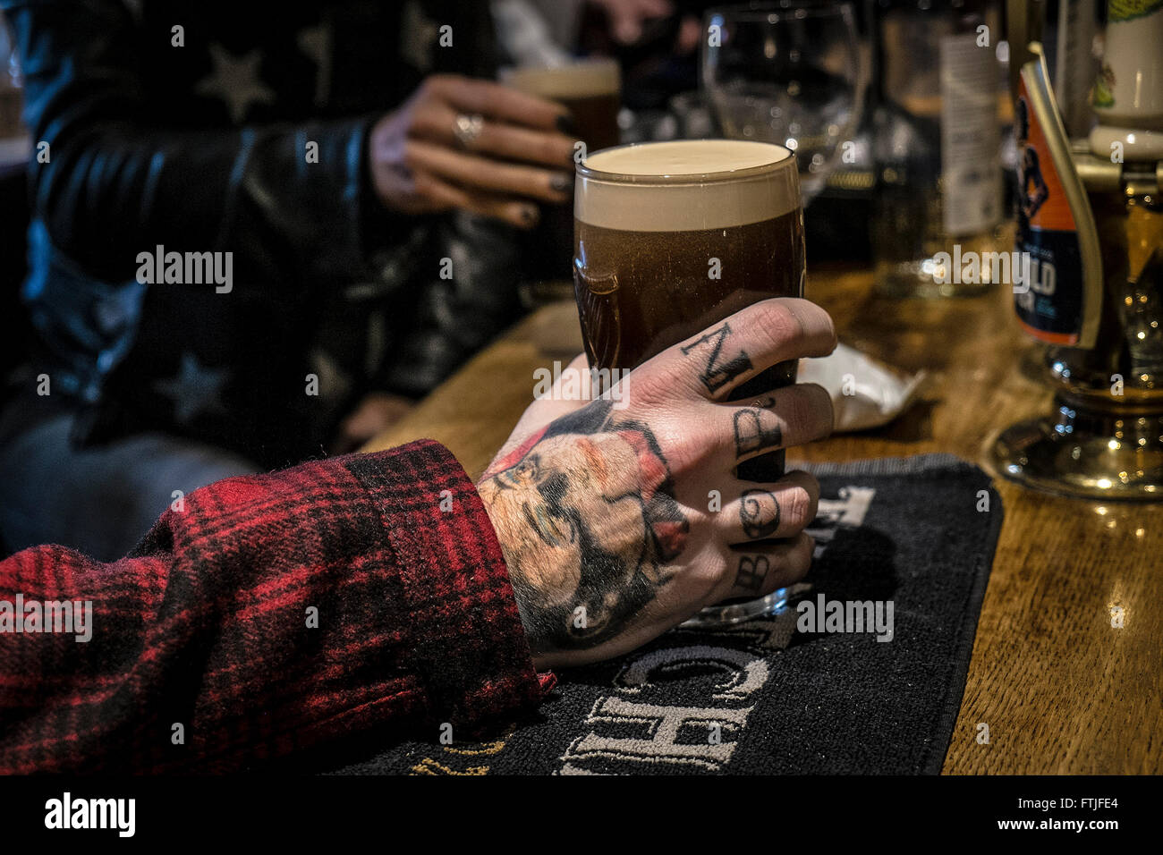 Une main tatouée du client avec une pinte de Guinness dans un pub anglais traditionnel dans l'Essex. Banque D'Images