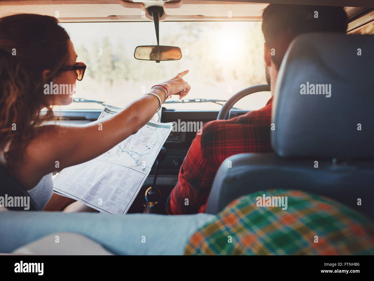 Vue arrière photo de couple de la conduite sur route de campagne. Femme tenant la carte et montrant la route carte à son petit ami de conduire la voiture. Banque D'Images