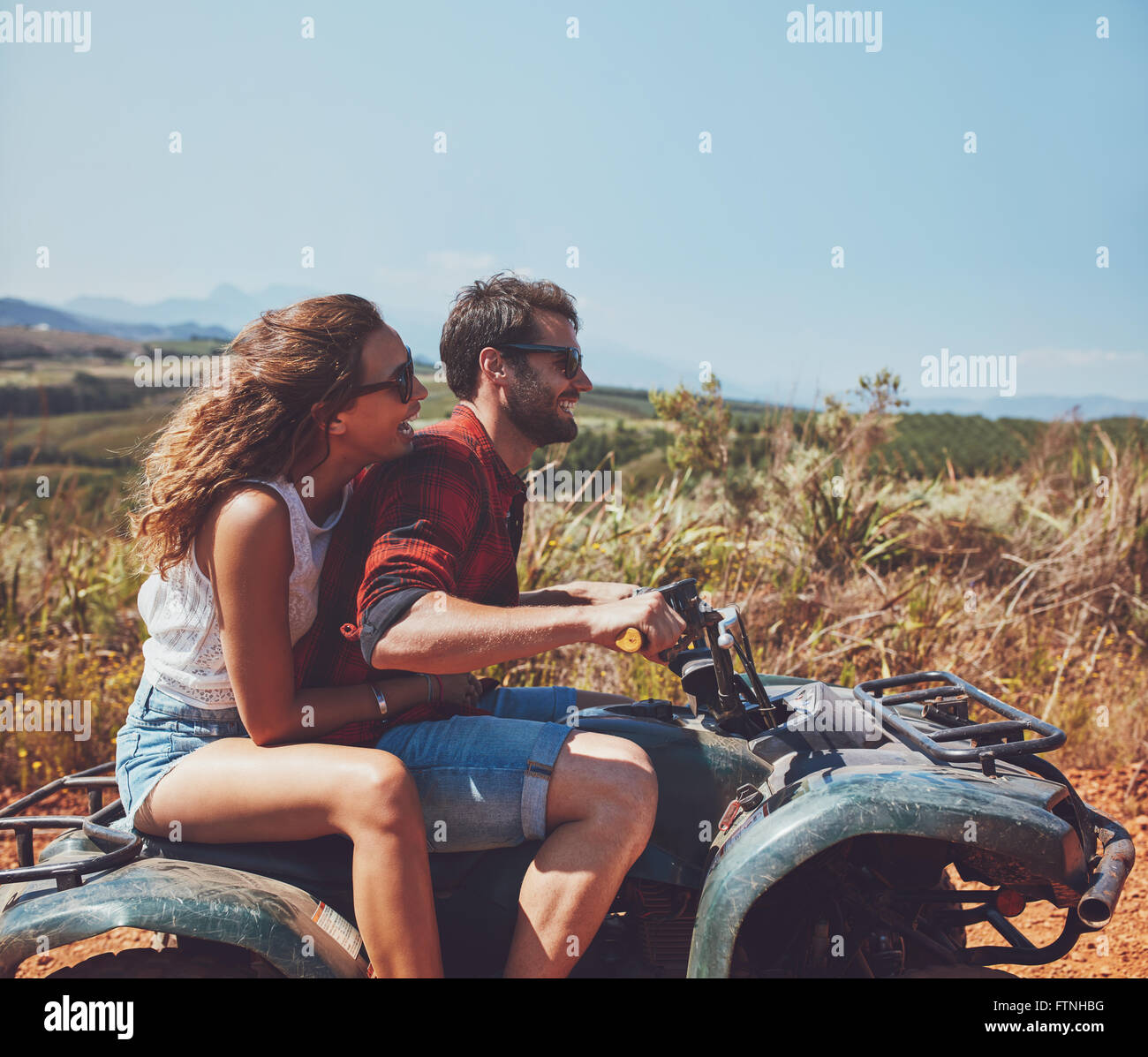 Side view of young man and woman riding sur un quad bike sur les vacances d'été. Couple vacances sur un quad en countrysi Banque D'Images