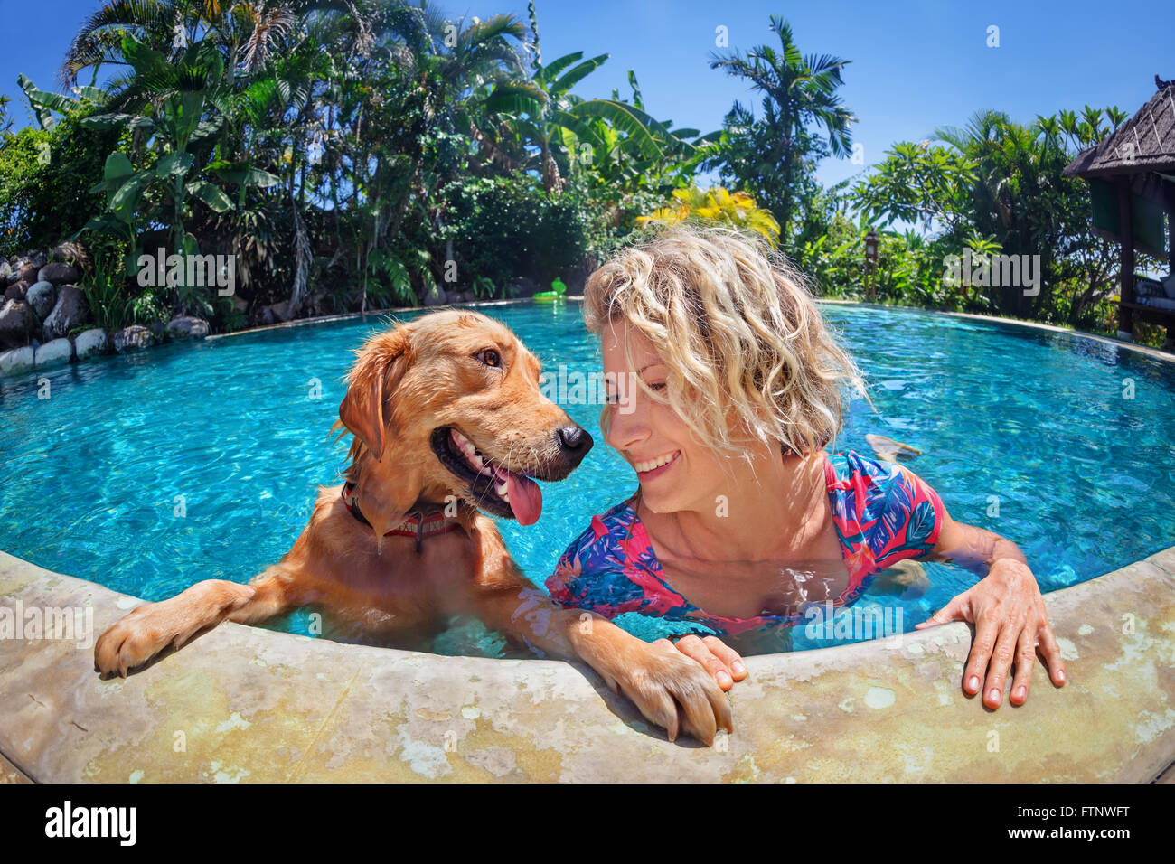 Portrait de femme smiley rigolo de jouer avec plaisir et de formation chiot golden retriever dans une piscine extérieure. Banque D'Images