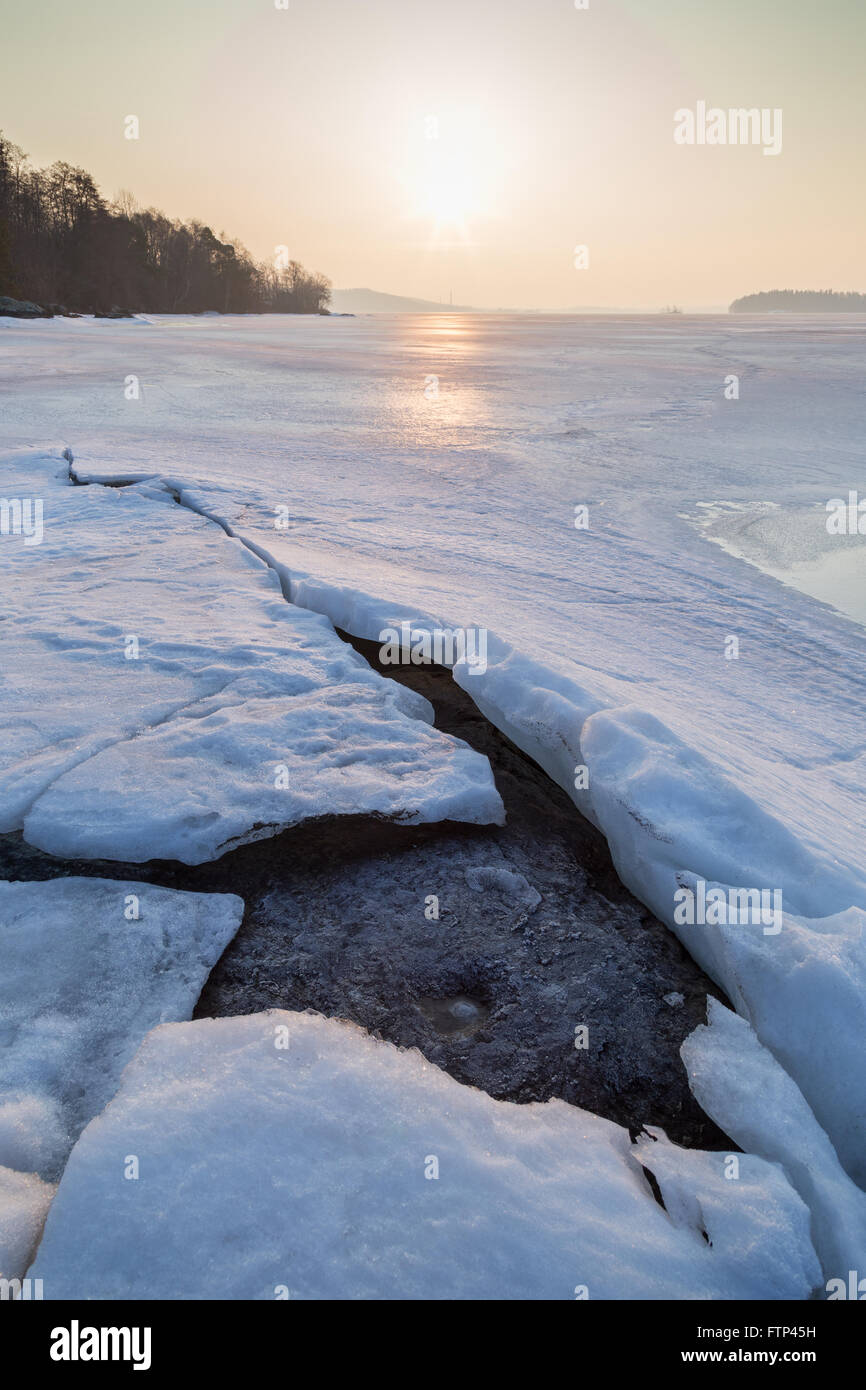 Roche sous la glace fissurée sur un lac gelé en Finlande au printemps, à l'aube. Banque D'Images