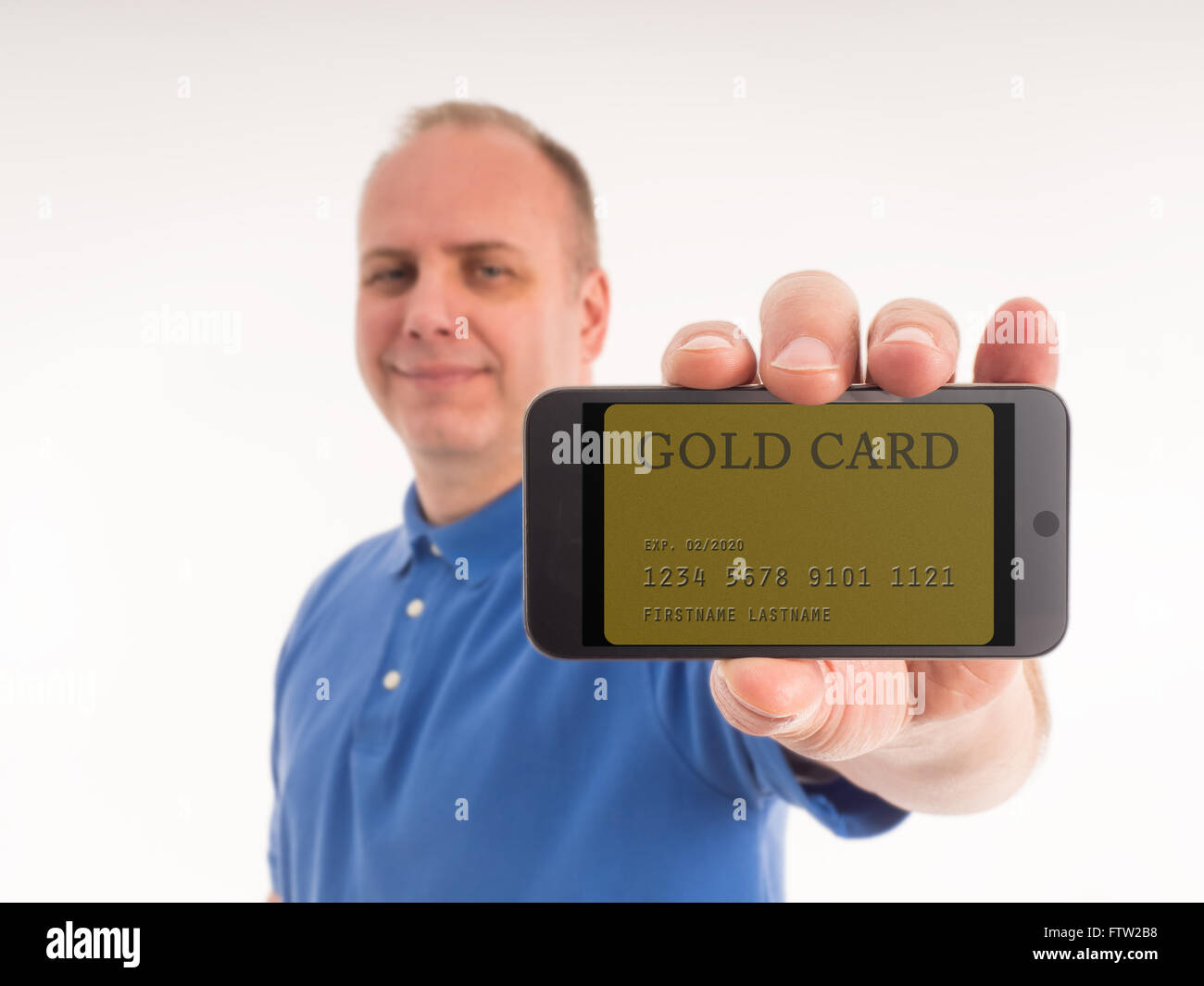 Un homme dans un polo bleu tient fièrement sur son téléphone intelligent, qui affiche une carte gold (carte de crédit) à l'écran. Le smart Banque D'Images