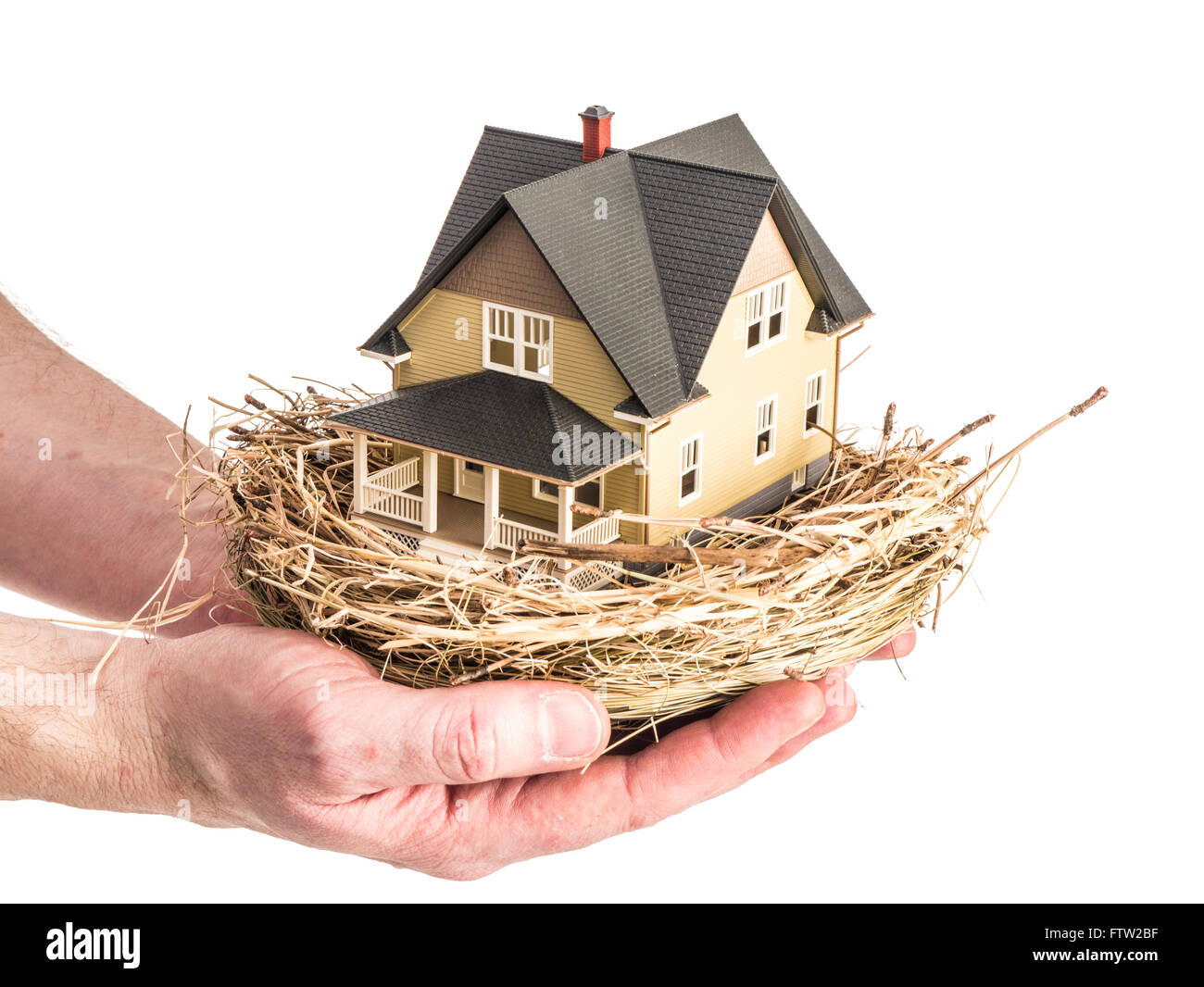 Photo d'un homme tenant un nid d'oiseau avec une miniature à l'intérieur de la maison, illustrant le concept d'investissement immobilier. Banque D'Images