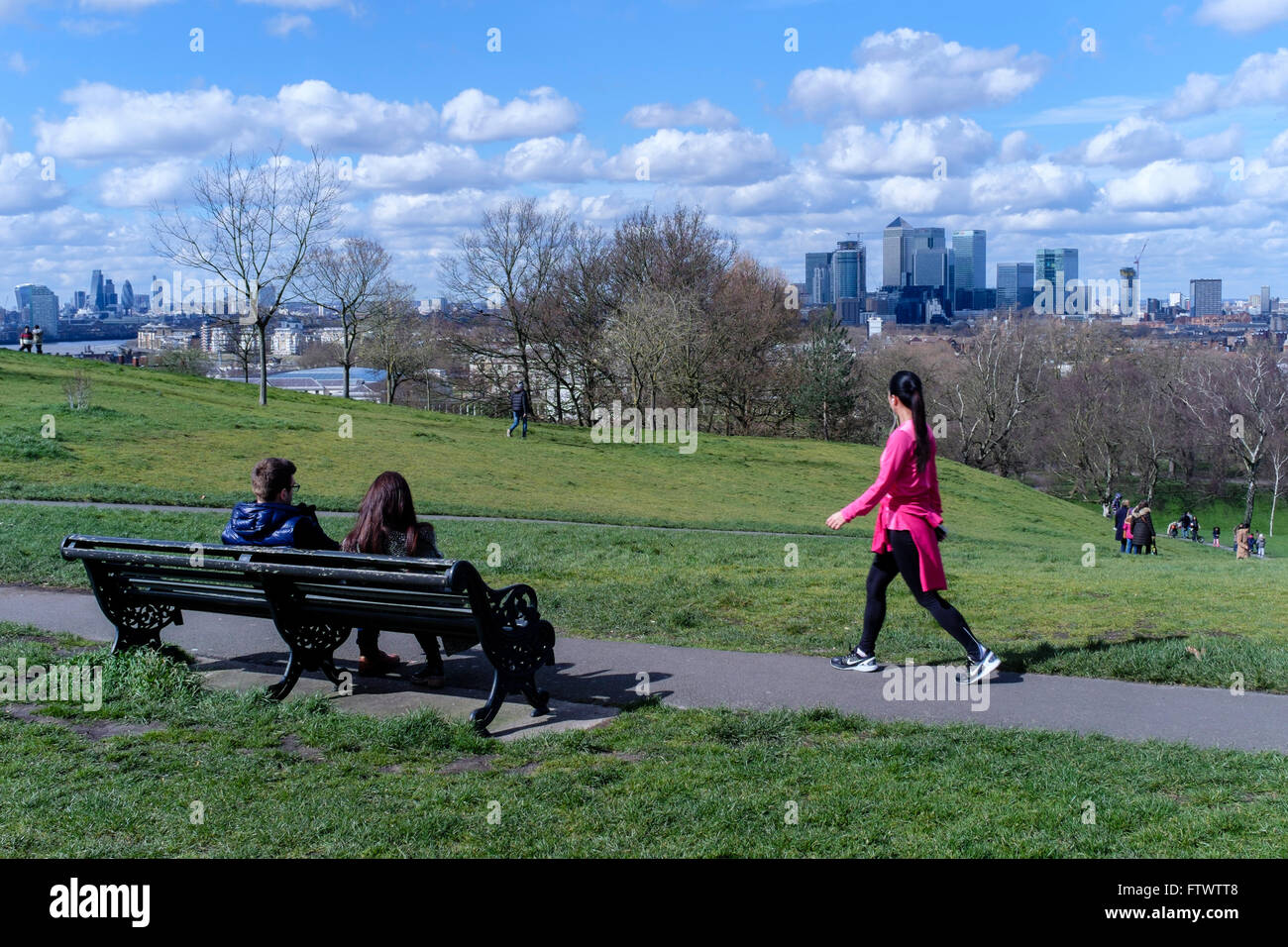 Jeune femme dans des vêtements d'exercice marche dernières couple sitting on bench, le Parc de Greenwich, London, UK Banque D'Images