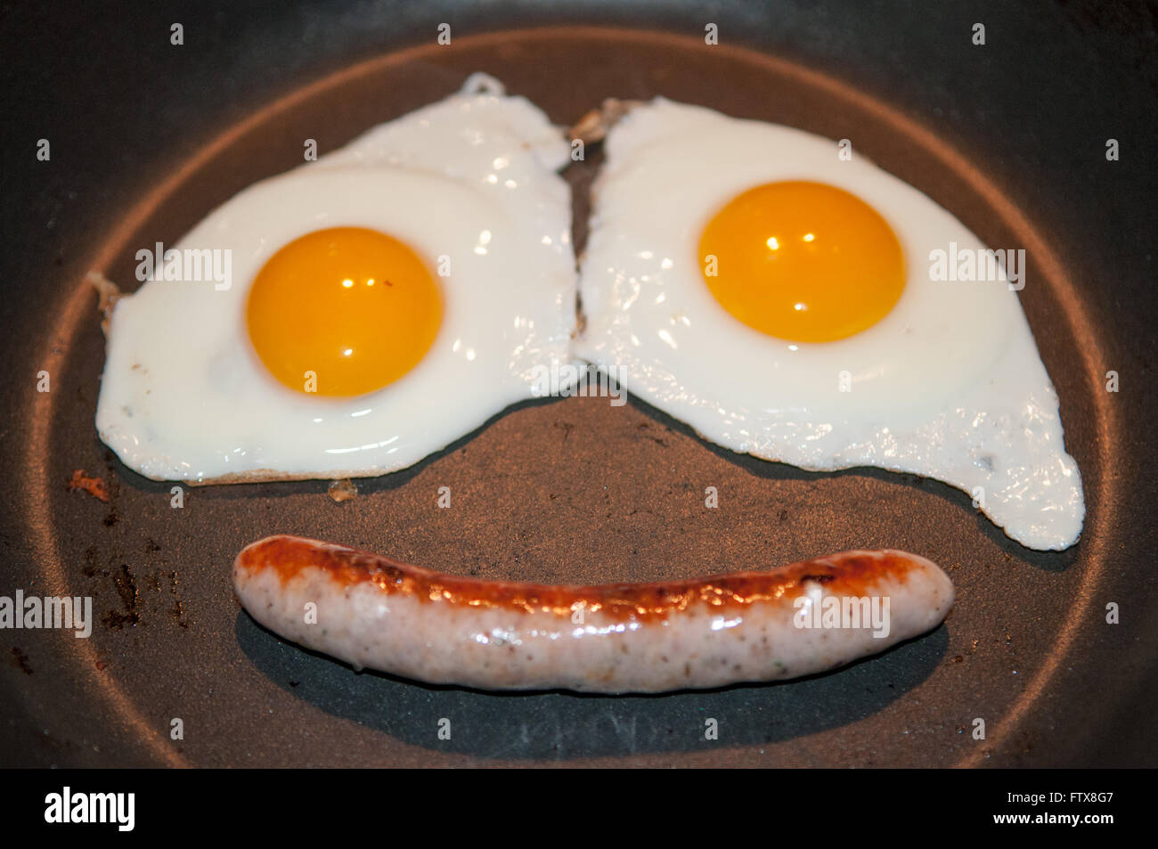 Deux œufs au plat et d'une saucisse faire un visage dans la casserole Banque D'Images