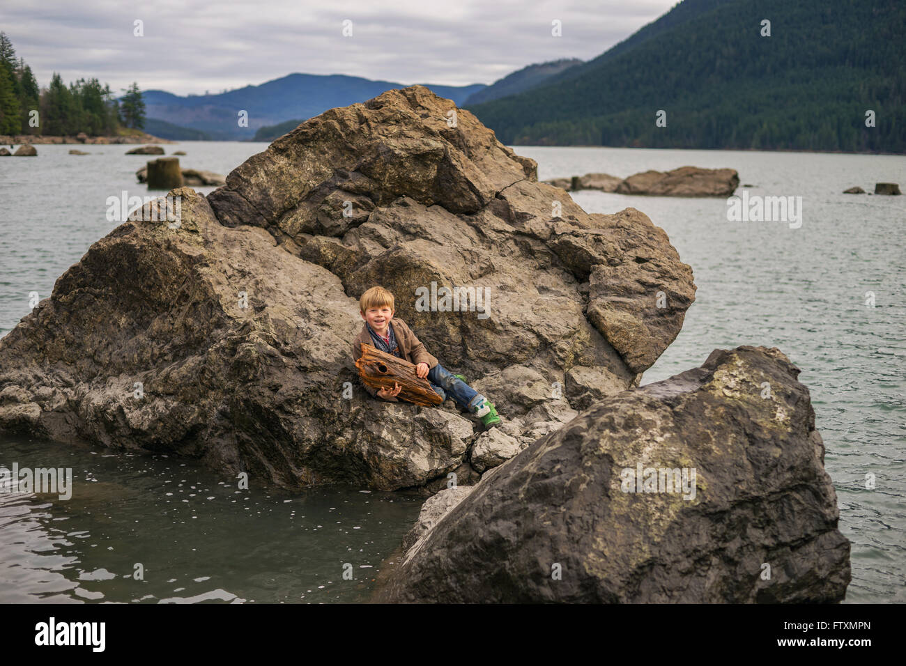 Garçon assis sur le gros rocher dans un lac Banque D'Images