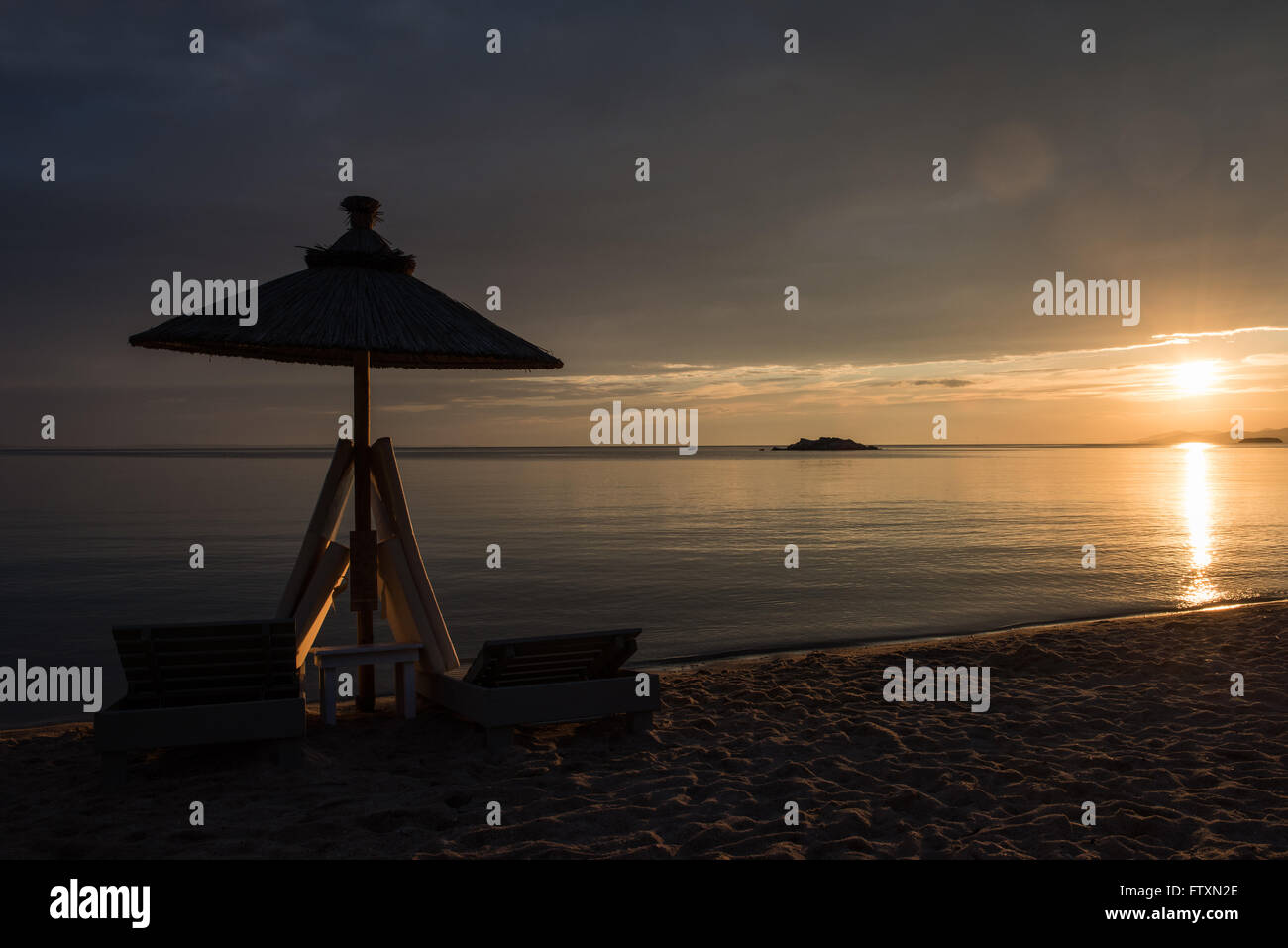 Silhouette d'un parasol et chaises longues sur la plage au coucher du soleil, la Grèce Banque D'Images