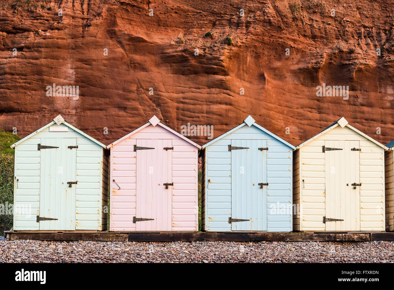 Beach Hut ligne dans des couleurs pastel, red rock fond, dans le sud du Devon, UK Banque D'Images