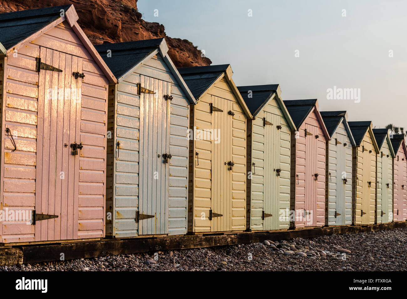 Beach Hut ligne dans des couleurs pastel, red rock fond, dans le sud du Devon, UK Banque D'Images