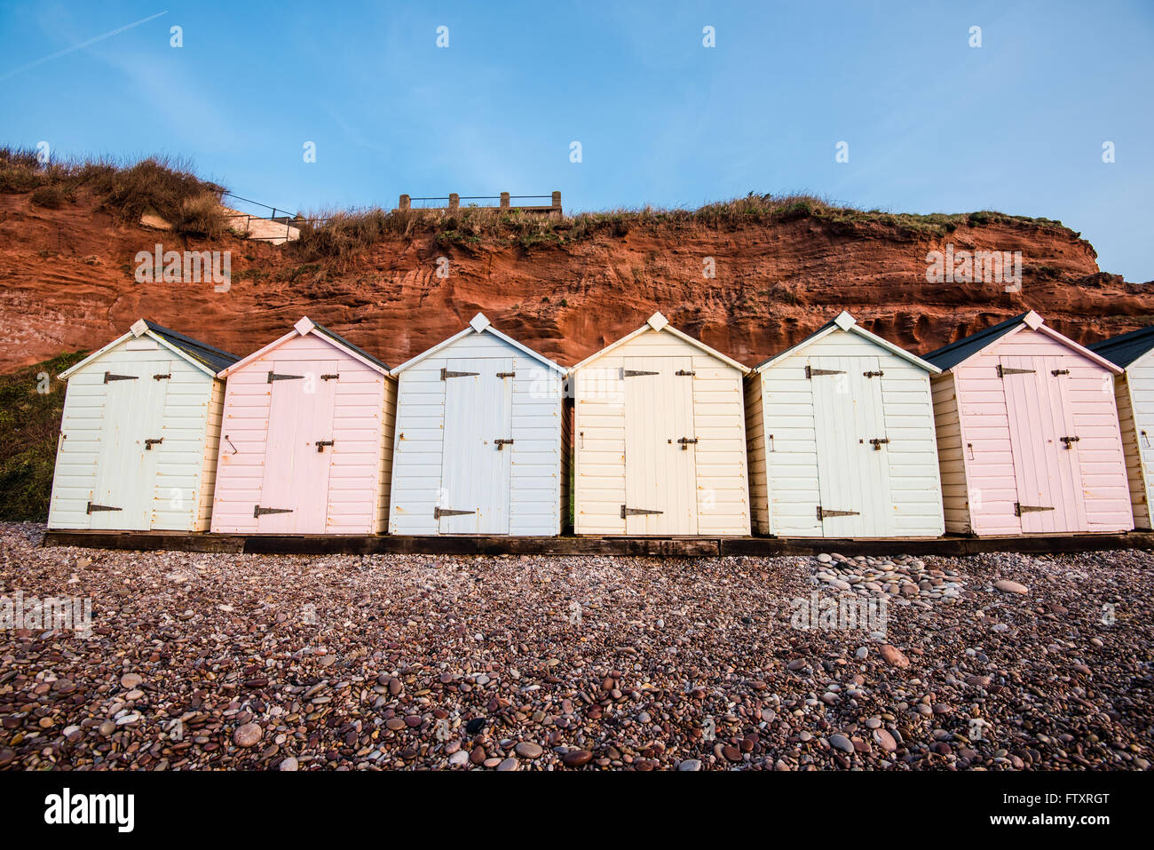 Beach Hut ligne dans des couleurs pastel, red rock cliff arrière-plan, dans le sud du Devon, UK Banque D'Images
