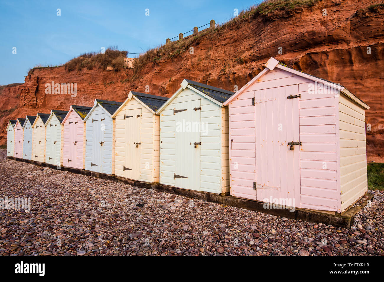 Beach Hut ligne dans des couleurs pastel, red rock cliff arrière-plan, dans le sud du Devon, UK Banque D'Images