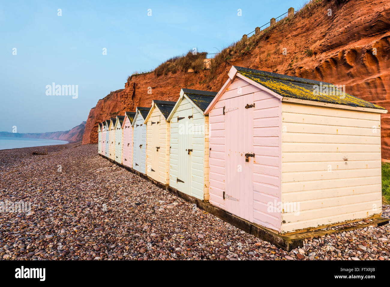 Beach Hut ligne dans des couleurs pastel, red rock cliff arrière-plan, dans le sud du Devon, UK Banque D'Images