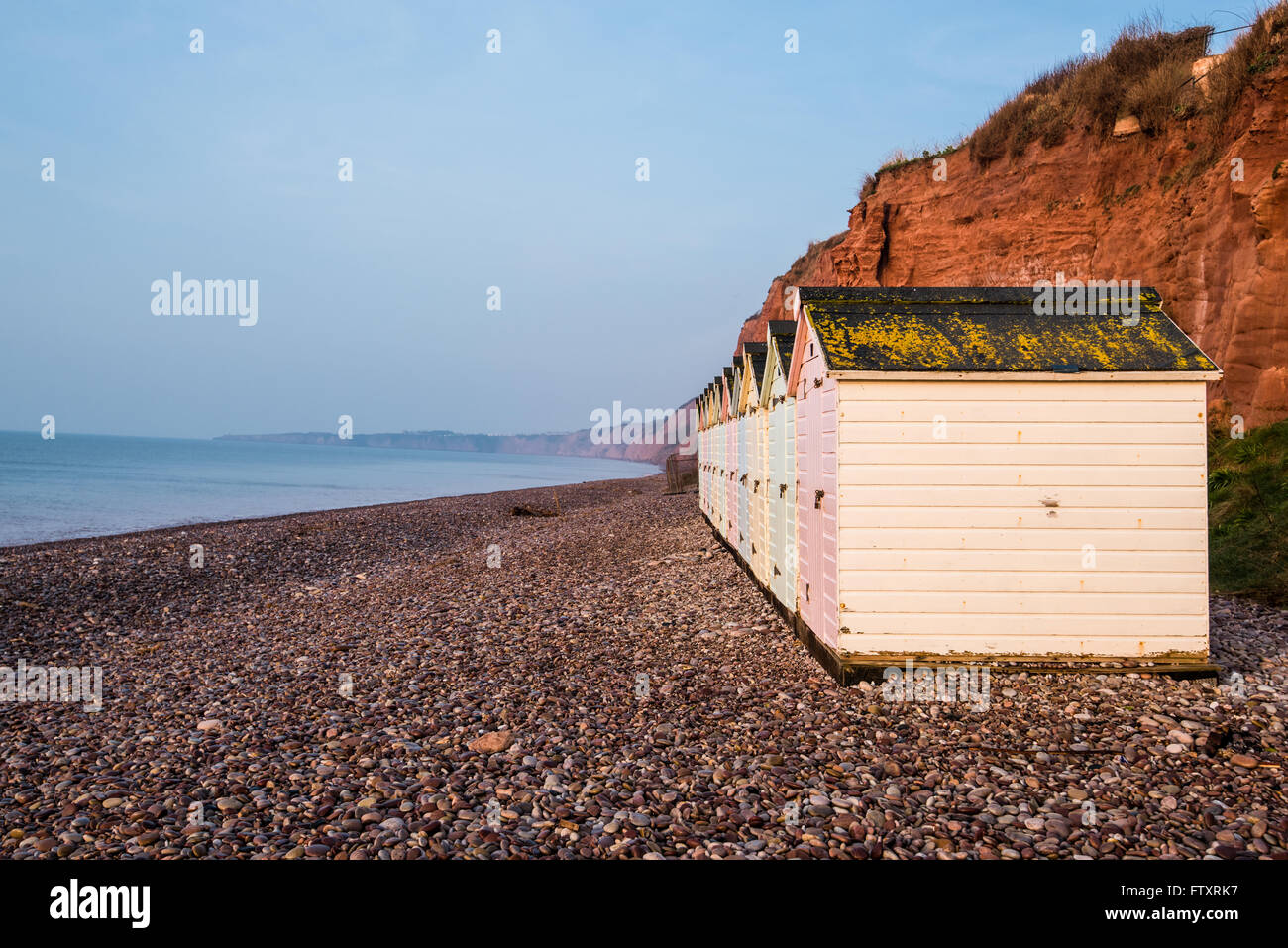 Beach Hut ligne dans des couleurs pastel, red rock cliff arrière-plan, dans le sud du Devon, UK Banque D'Images